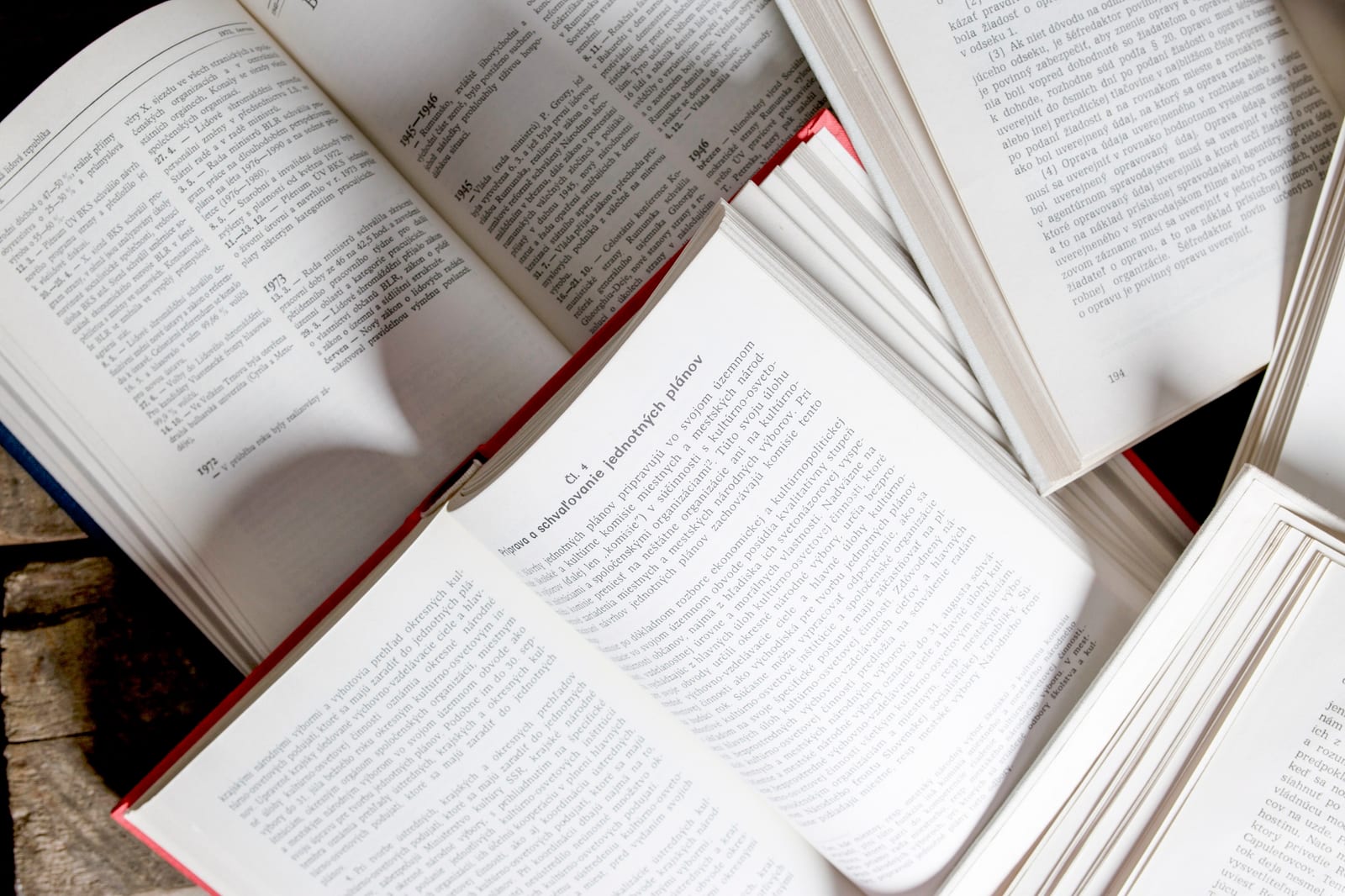 Livros abertos e empilhados sobre uma mesa, mostrando páginas de texto denso lado a lado