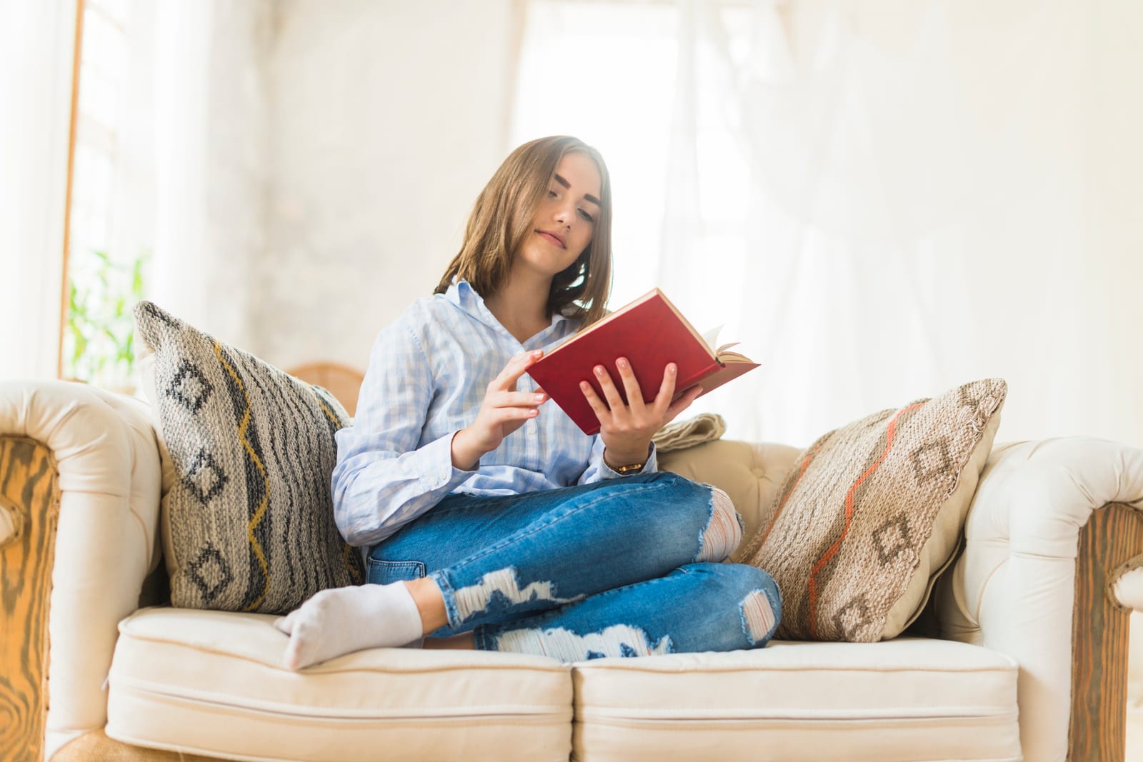 Leitora sentada em um sofá claro, com um livro de capa vermelha aberto nas mãos