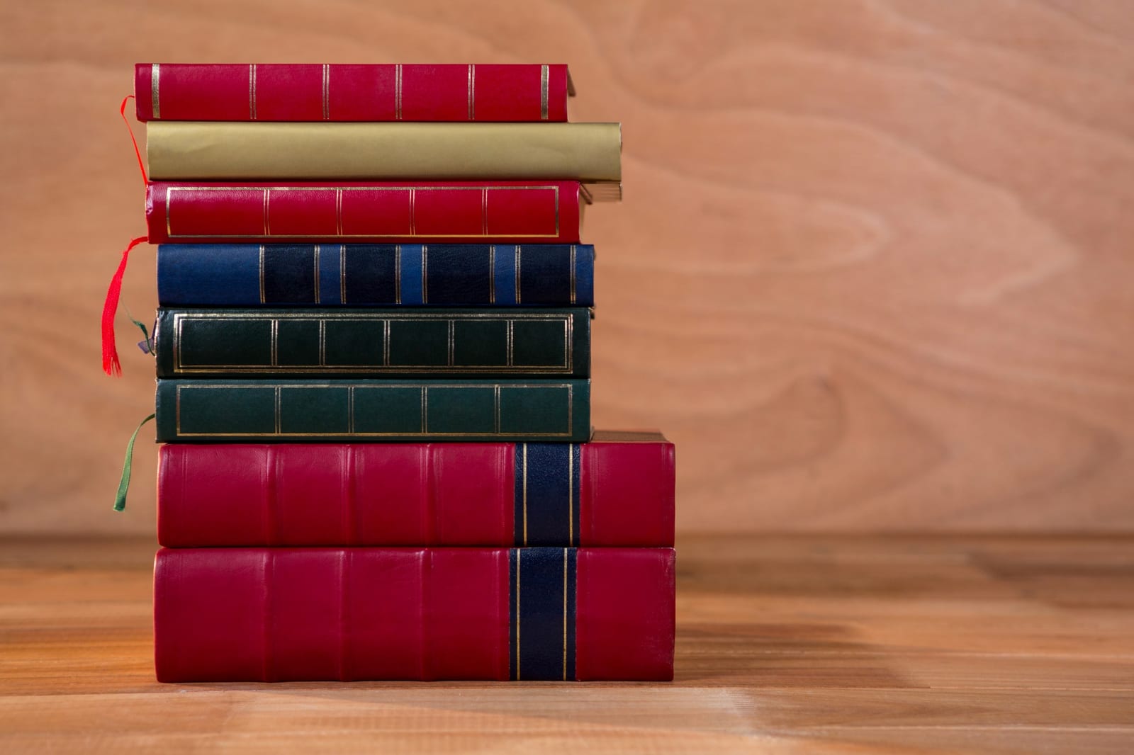 Pilha de livros encadernados em tons de vermelho, azul e verde, com uma fita vermelha marcando as páginas